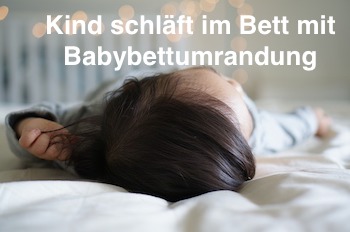Kind schläft im Bett mit Babybettumrandung